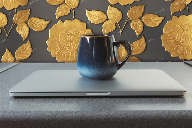 Embossed Gold Flowers Wallpaper pattern with blue coffee mug sitting on closed laptop